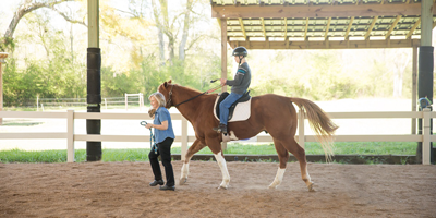 A Special Equestrians team member leads a child around a rink on a horse.