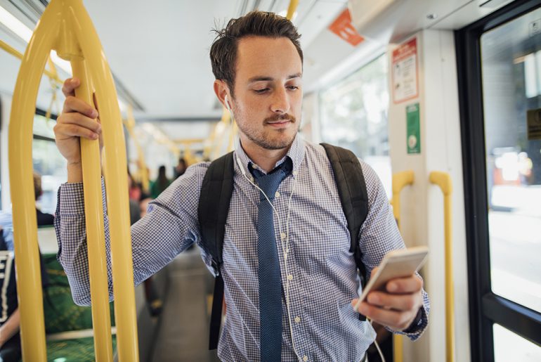 A man riding the subway, looking at his phone, as if on his way to work. 