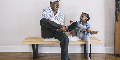 Older black man sitting on a bench and laughing with young granddaughter