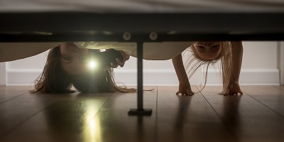 Two little girls looking under the bed with a flashlight