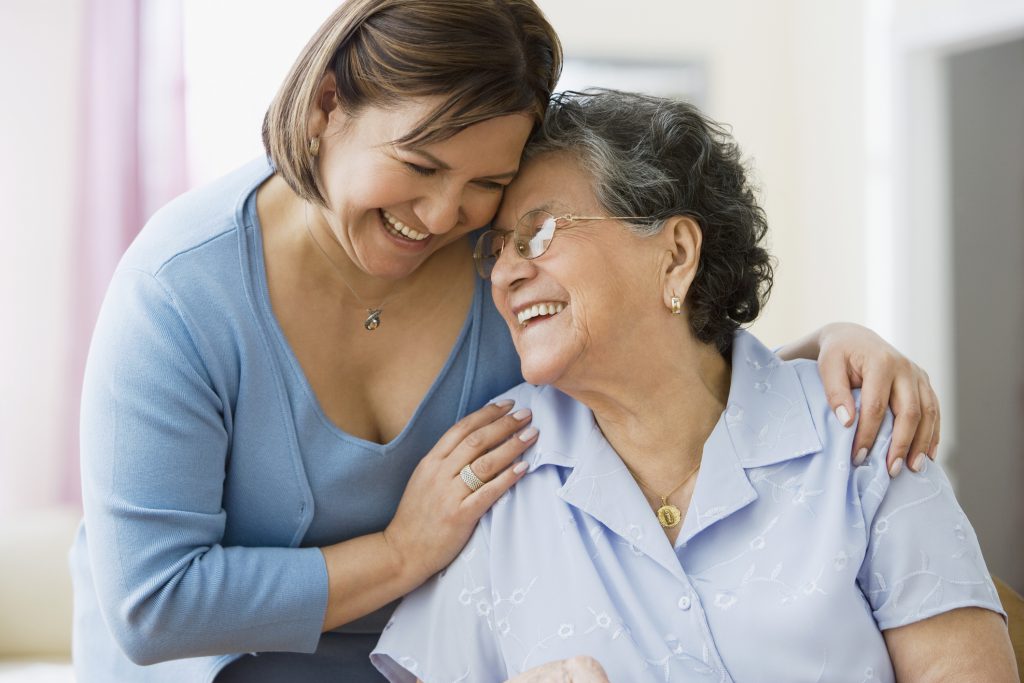 An adult daughter hugging her elderly mom, both of them smiling.