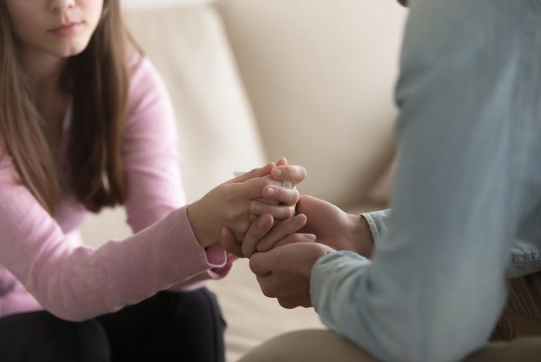 Partial image of young woman and a man reaching across the table to grab her hands in support.