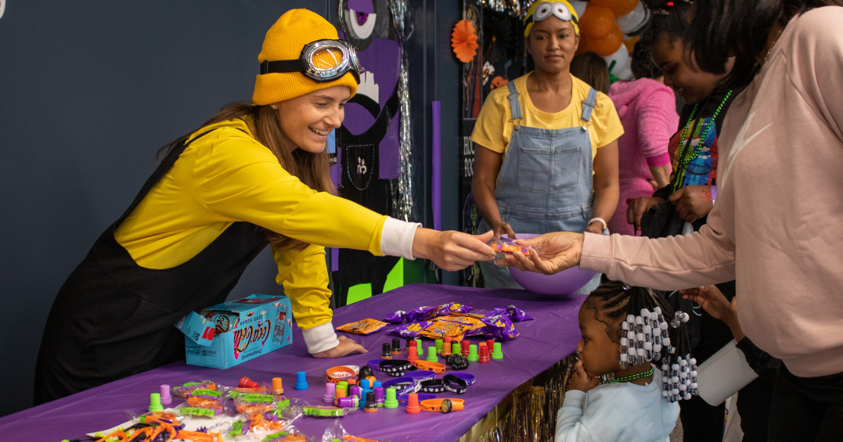 Protective volunteer dressed as a Minion handing candy to a child and parent